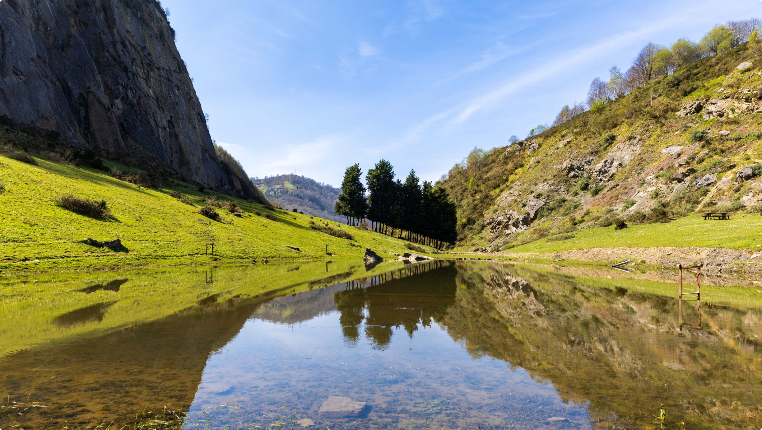 Paisaje natural con un lago reflejando árboles y montañas bajo un cielo azul