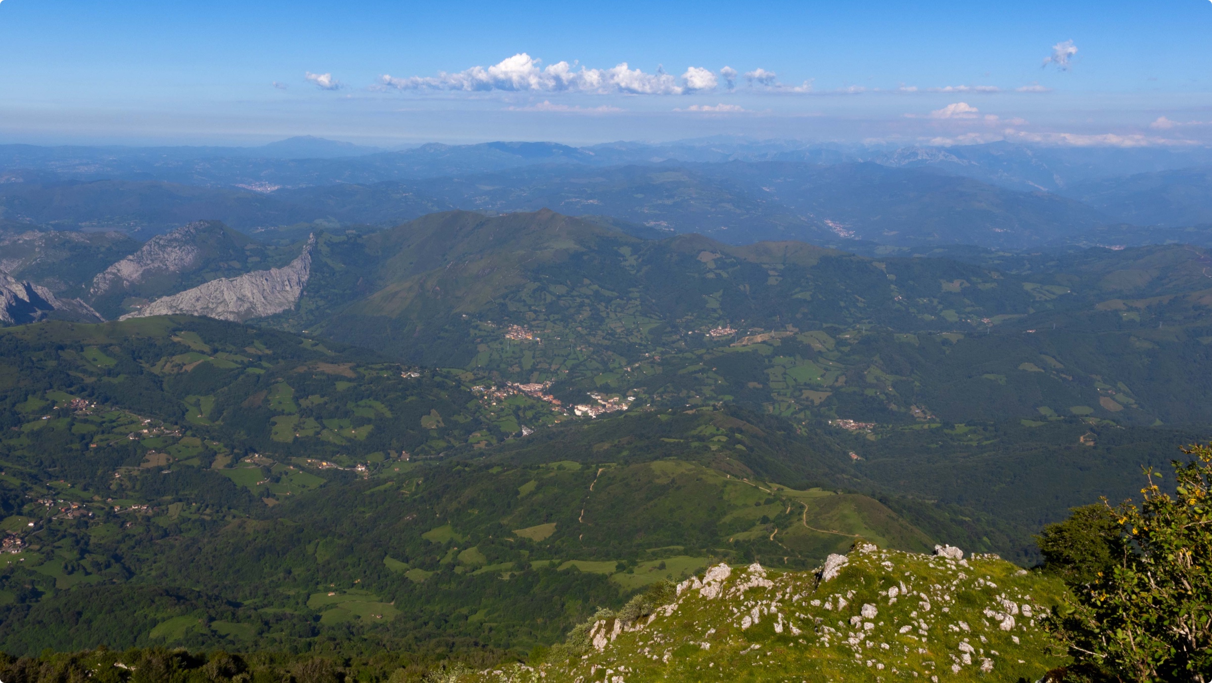 Panorámica de montañas y valles verdes bajo un cielo azul con algunas nubes