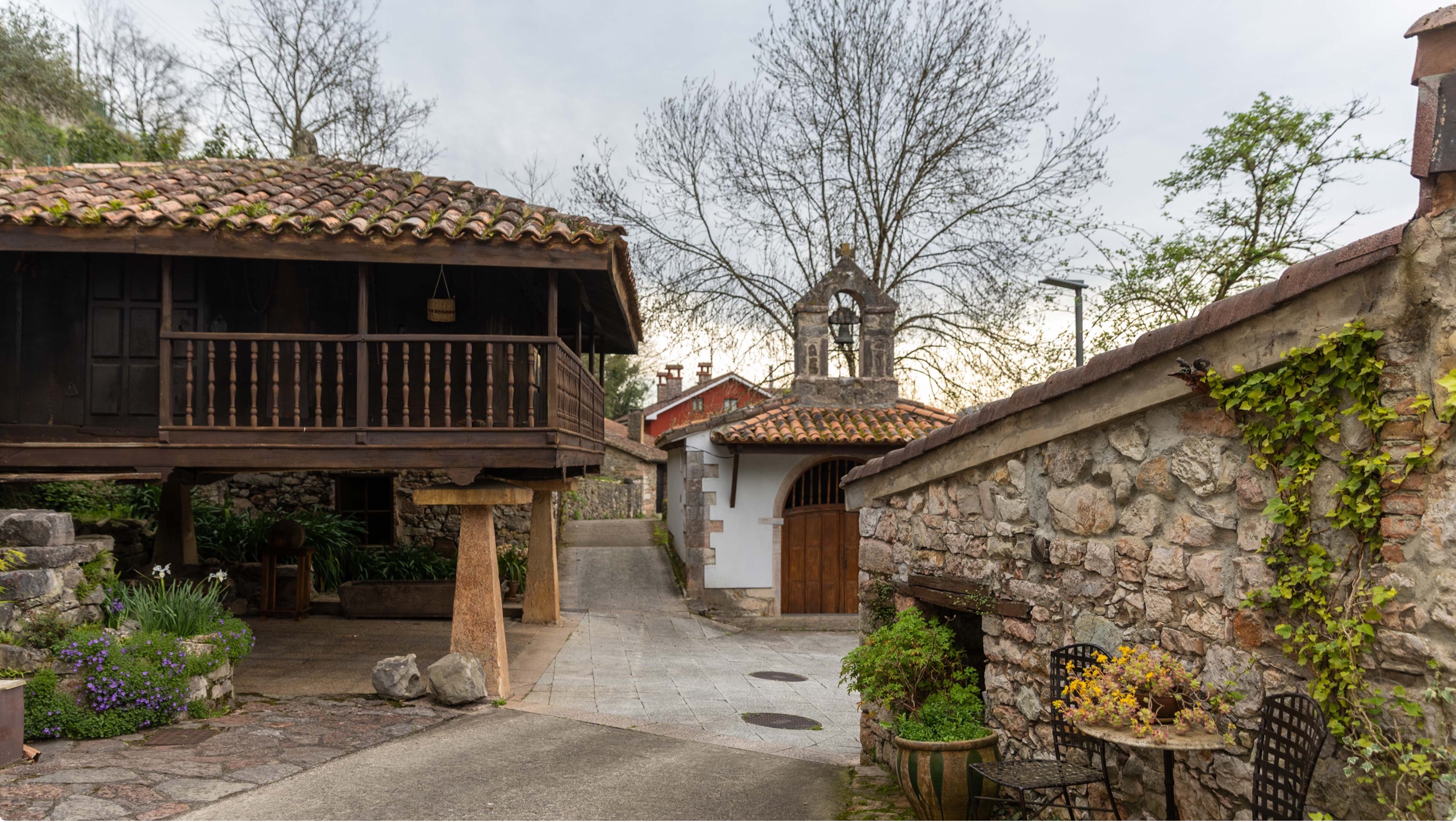 Vista de un camino en un pueblo con casas de piedra y un campanario al fondo