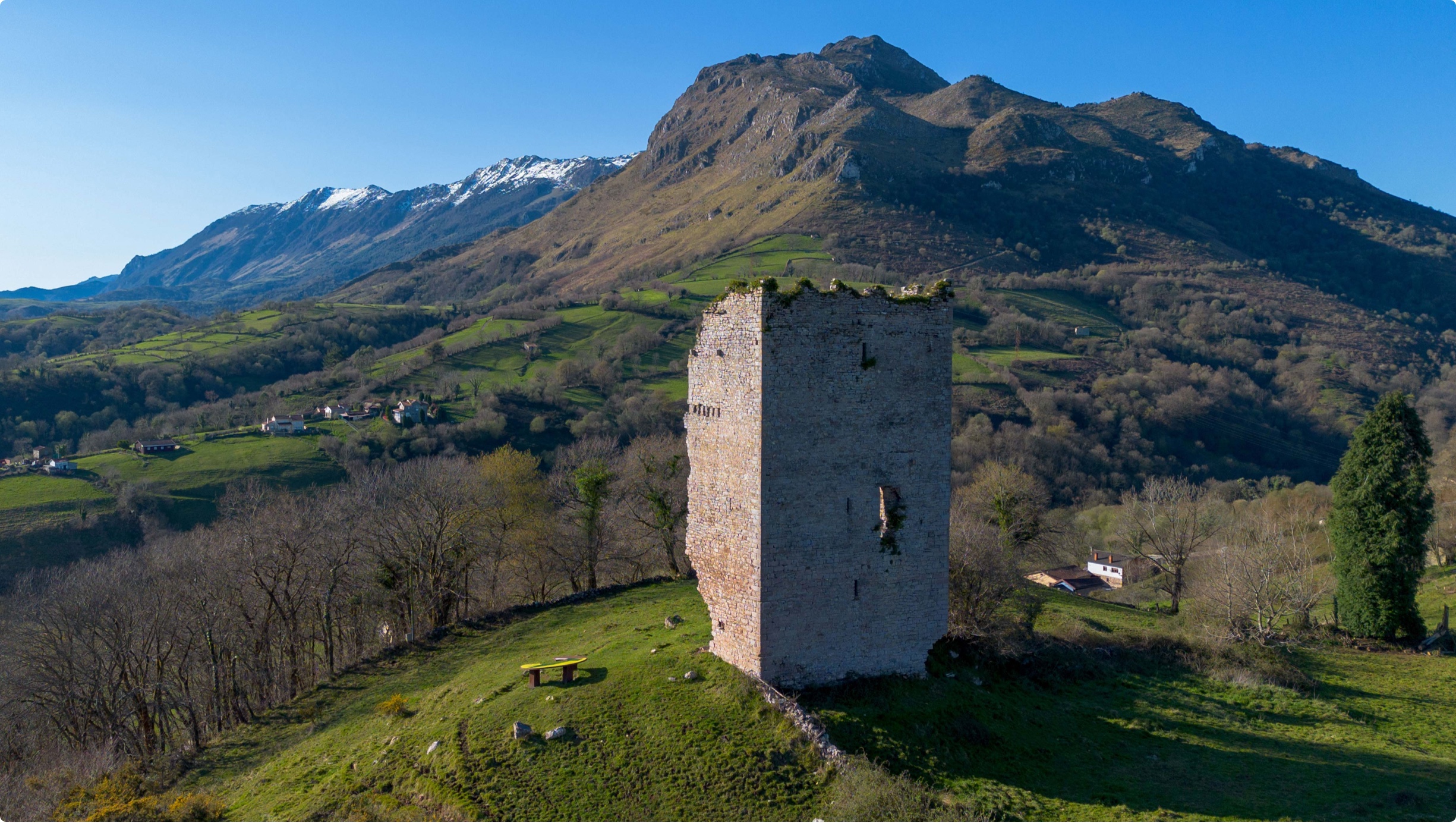 Torre de piedra en un paisaje montañoso con vegetación y nieve en las cumbres