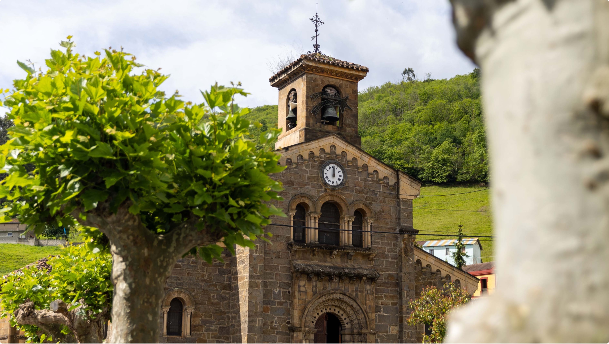 Iglesia de estilo arquitectónico tradicional con campanario y reloj, rodeada de vegetación