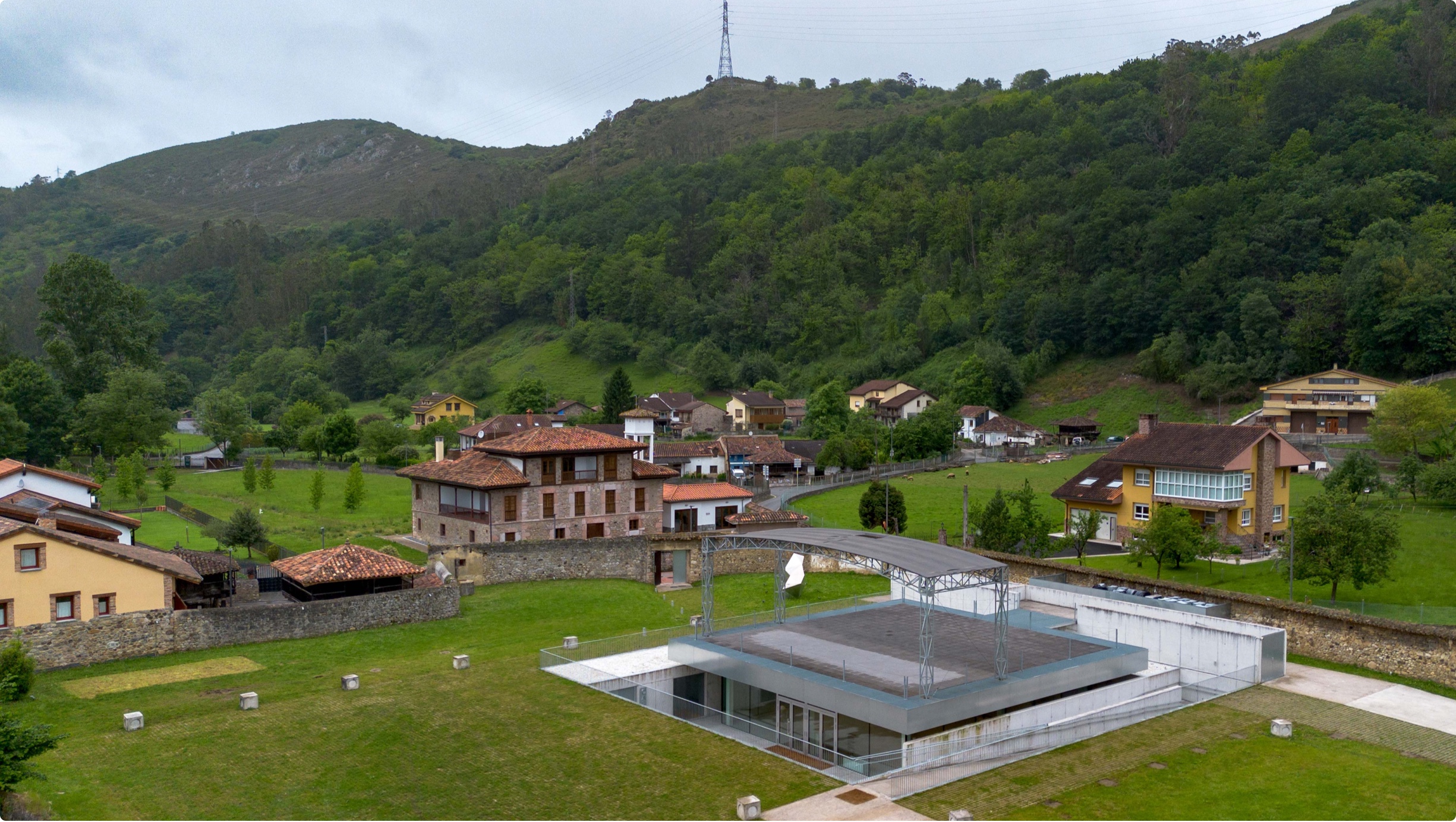 Vista panorámica de un edificio moderno en un paisaje rural con montañas y casas tradicionales