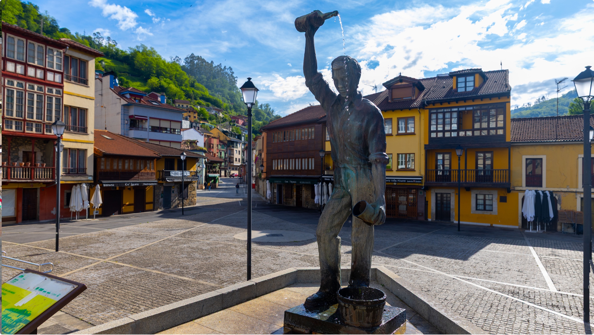 Estatua de un hombre vertiendo agua en una plaza con edificios coloridos al fondo