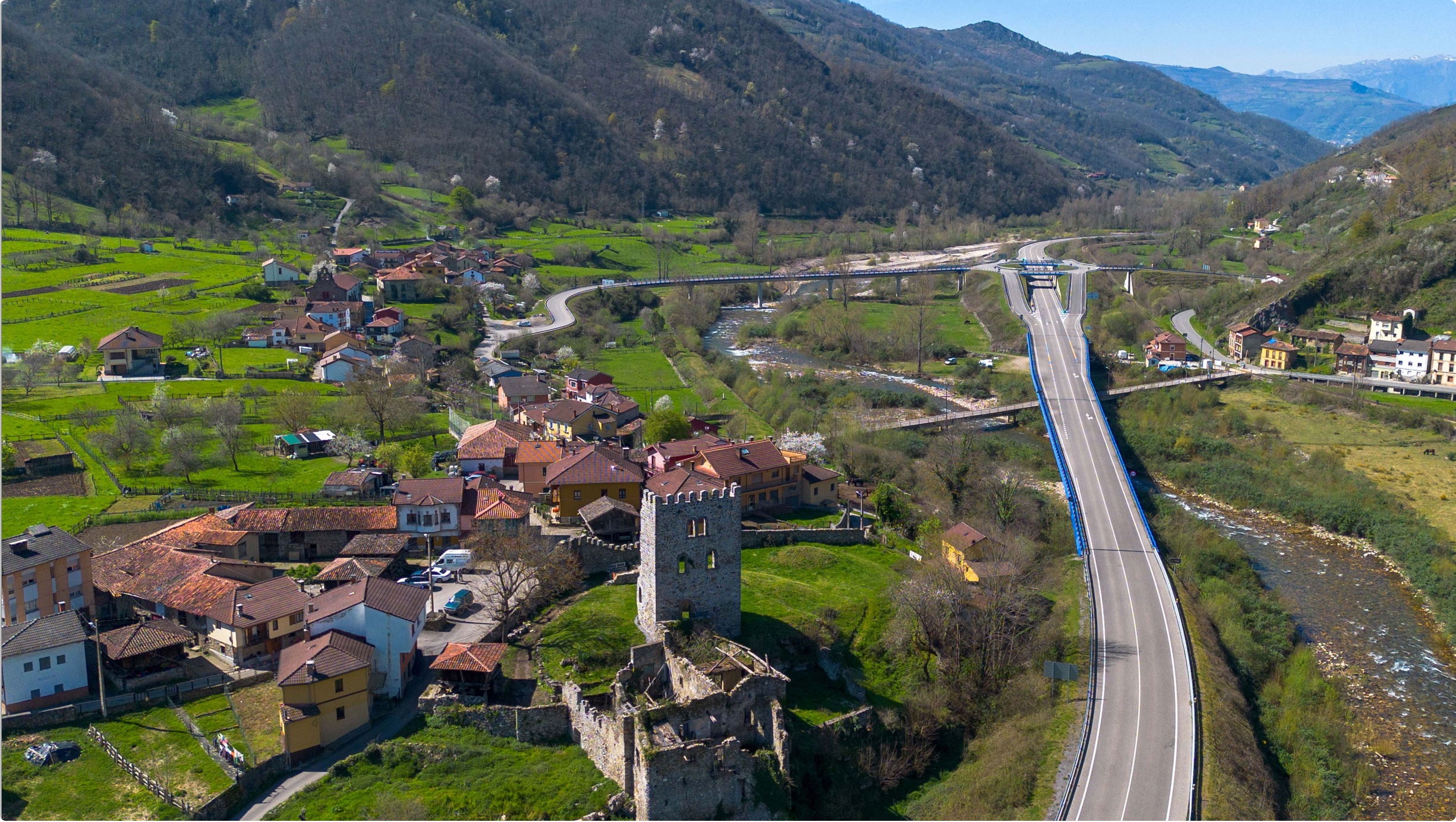 Vista aérea de un pueblo con casas de techos rojos, un castillo y una carretera que atraviesa un paisaje montañoso