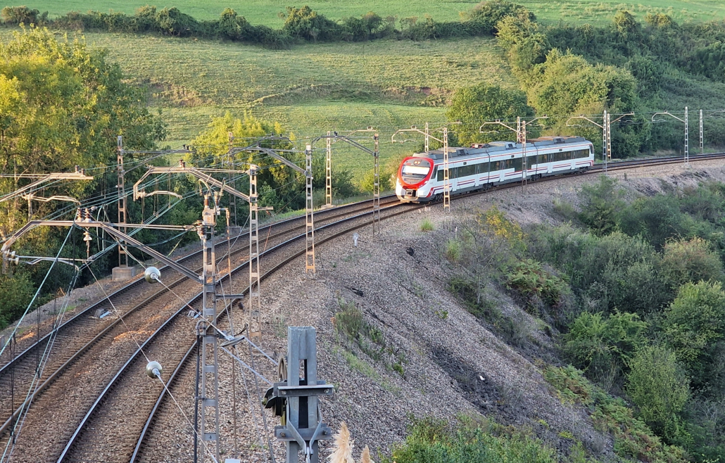 Tren circulando por una vía férrea en un paisaje verde y montañoso