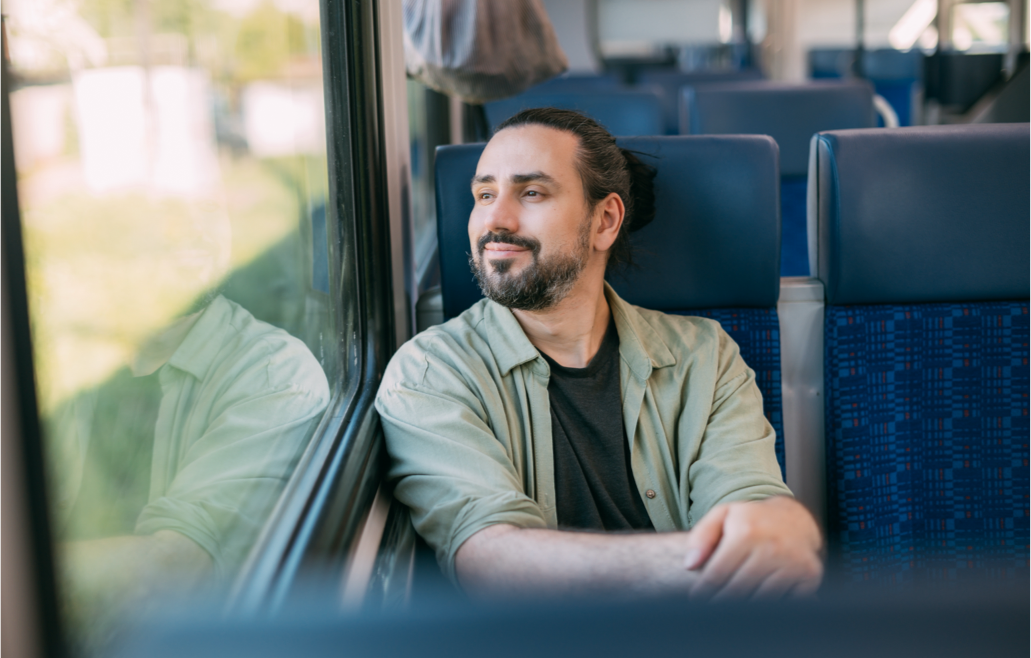 Hombre sentado en un tren, mirando por la ventana con una expresión tranquila