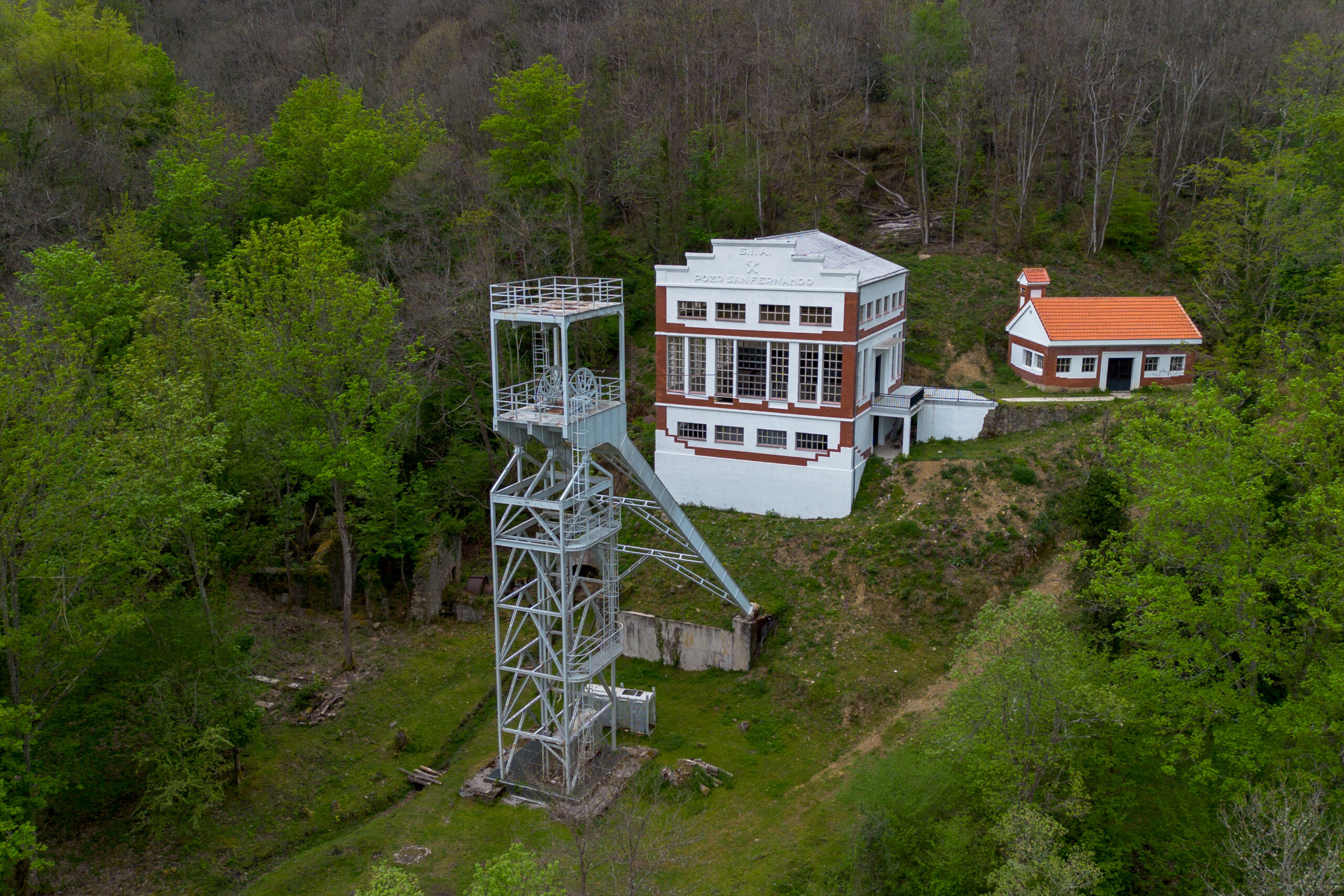 Edificio de estilo industrial con una estructura metálica al lado, rodeado de vegetación y árboles