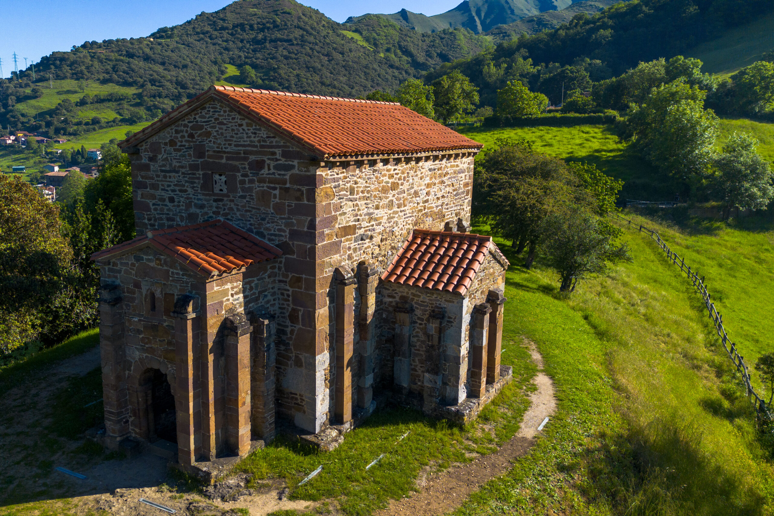Iglesia de estilo prerrománico rodeada de vegetación y montañas