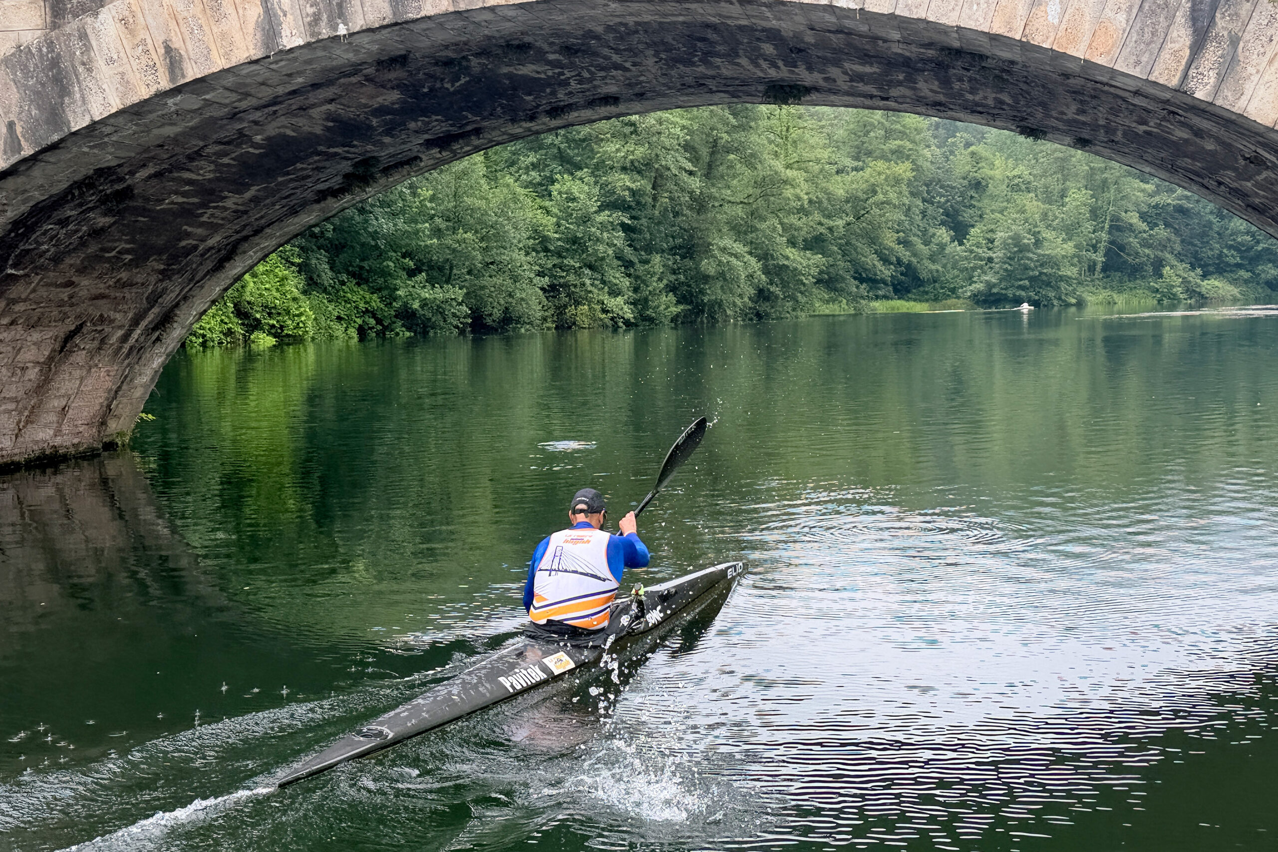 Un piragüista navega bajo un puente en un río rodeado de vegetación
