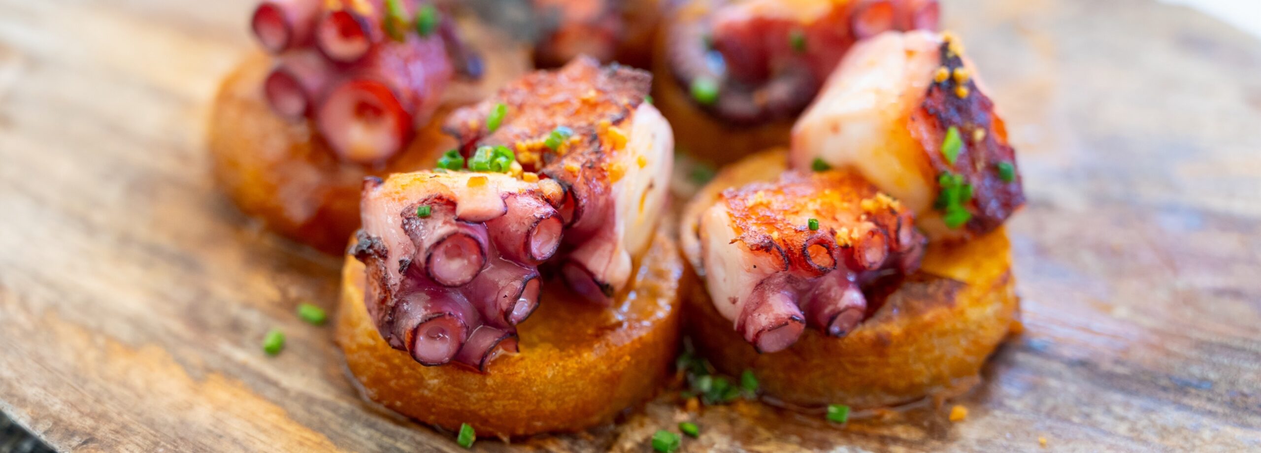Tostas de pulpo con pimientos y hierbas sobre una tabla de madera
