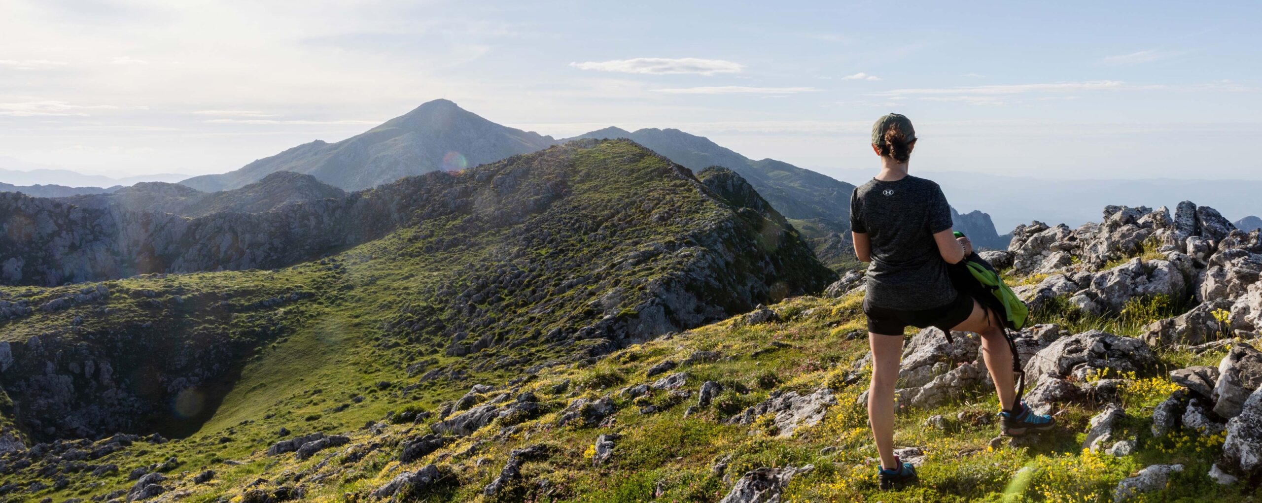 Persona de espaldas contemplando un paisaje montañoso con mar al fondo