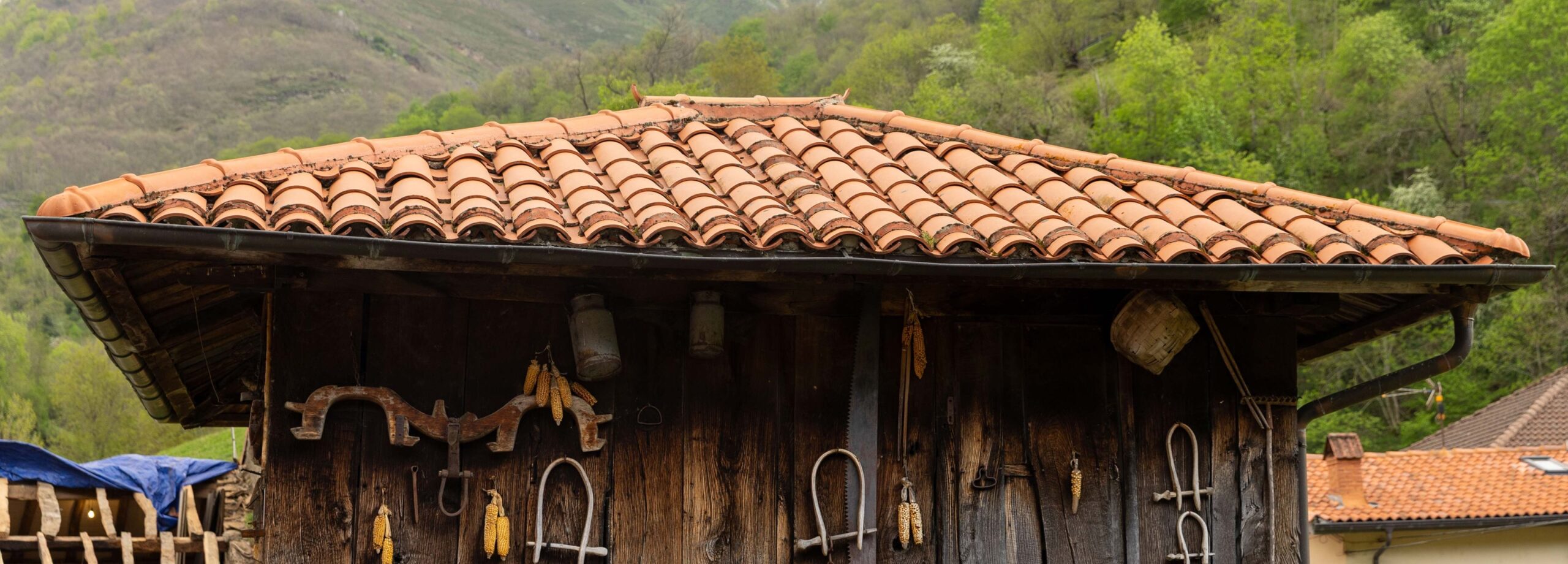 Tejado de tejas de un edificio rústico con herramientas colgadas en la pared y un paisaje montañoso al fondo