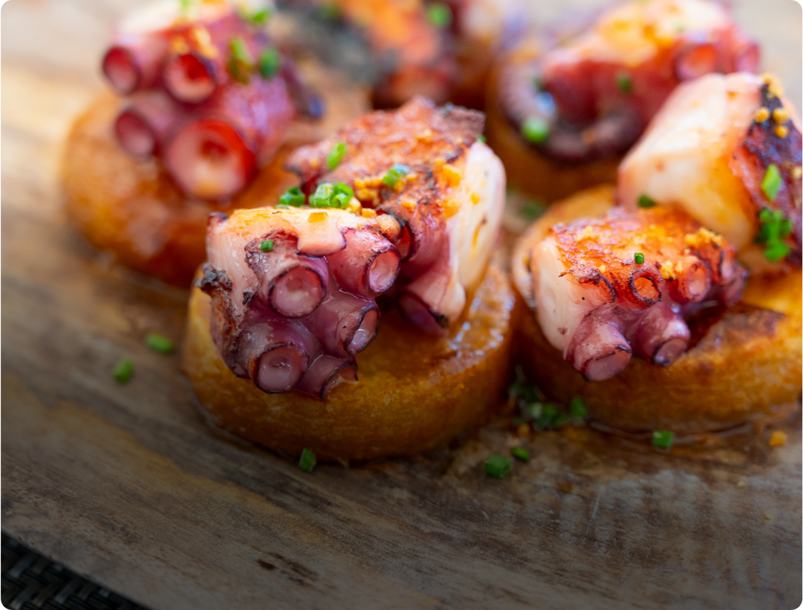 Trozos de pulpo asado sobre rodajas doradas de patata, decorados con cebollino