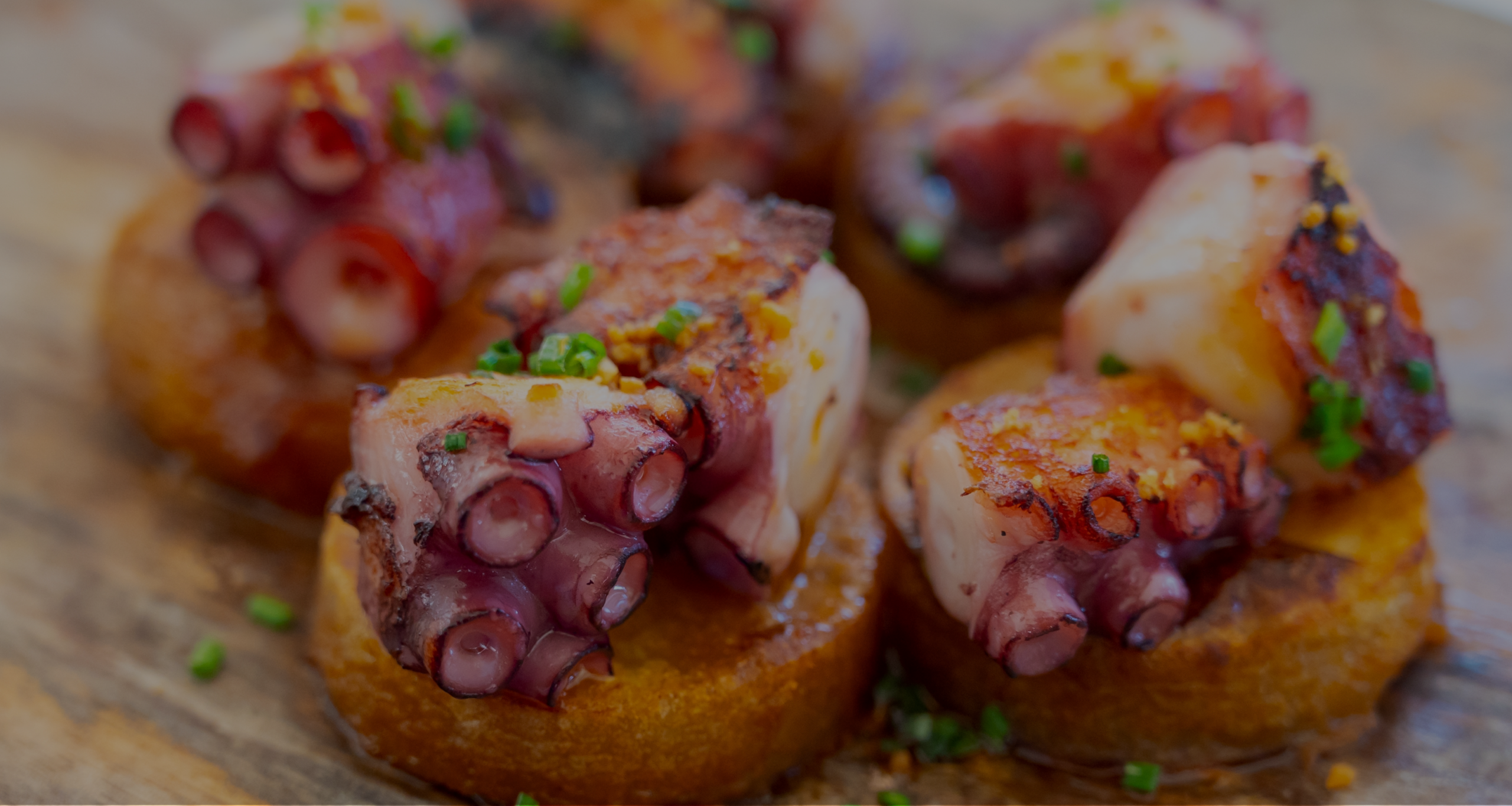 Trozos de pulpo asado sobre rodajas doradas de patata, decorados con cebollino