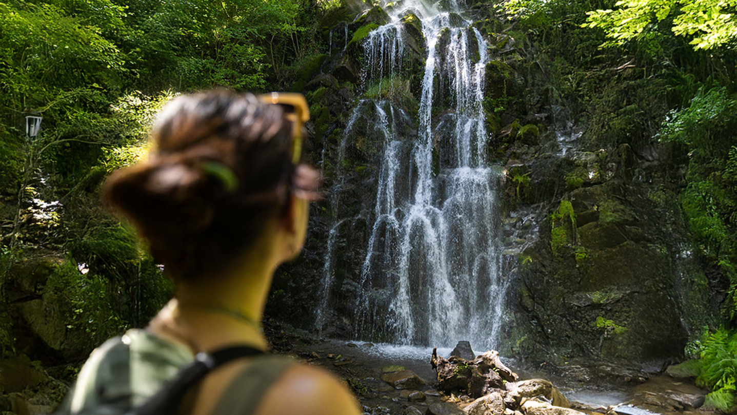 Mujer de espaldas contemplando una cascada rodeada de vegetación