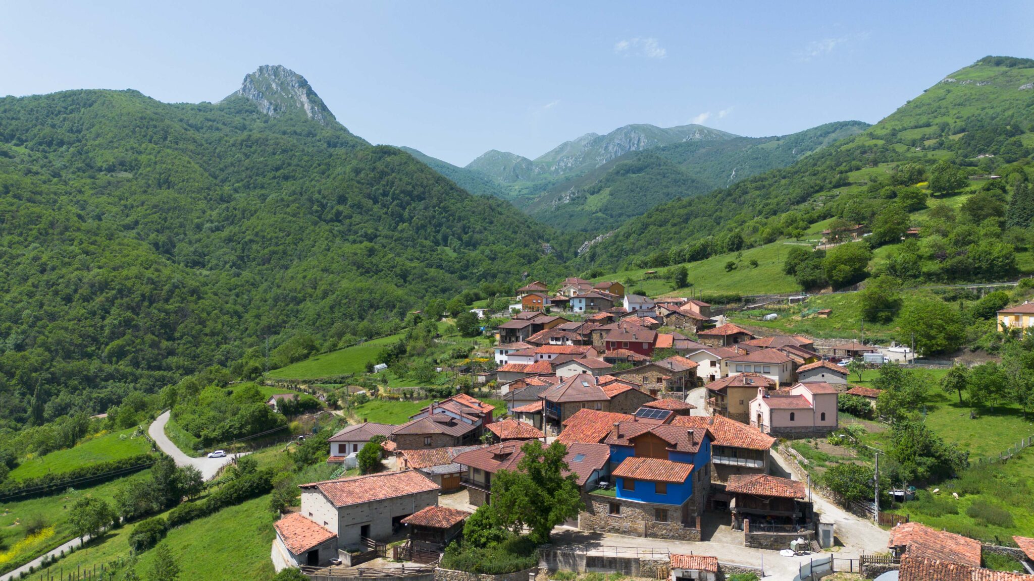 Vista panorámica de un pueblo rural con casas de techos rojos rodeado de montañas verdes