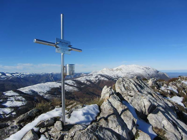 Cruz metálica en un paisaje montañoso nevado bajo un cielo azul despejado