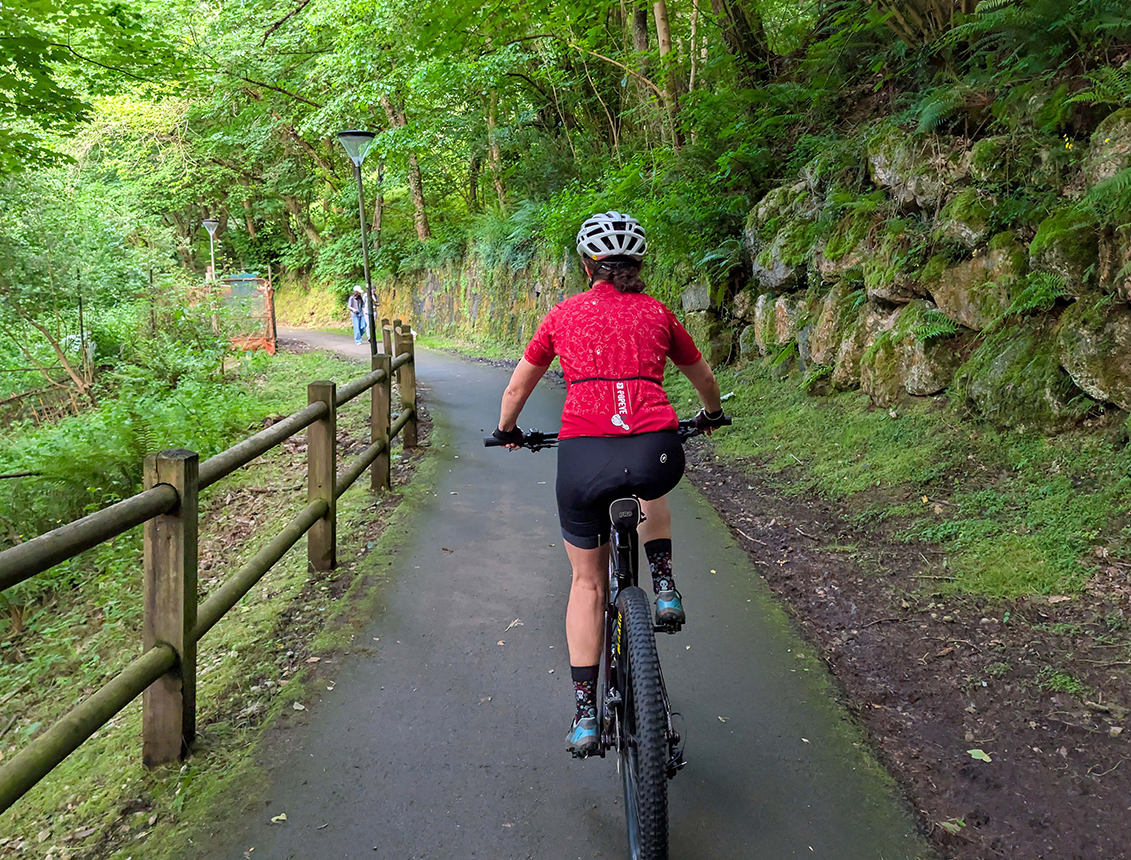 Ciclista montando por un sendero rodeado de vegetación y rocas