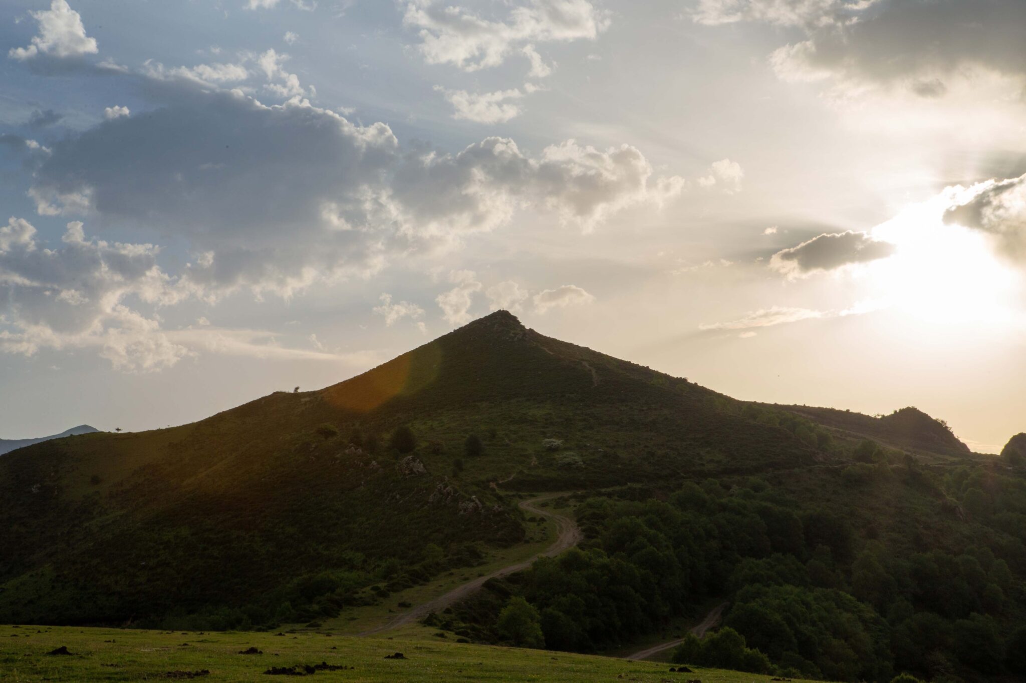 Montañas verdes bajo un cielo nublado con el sol brillando al fondo