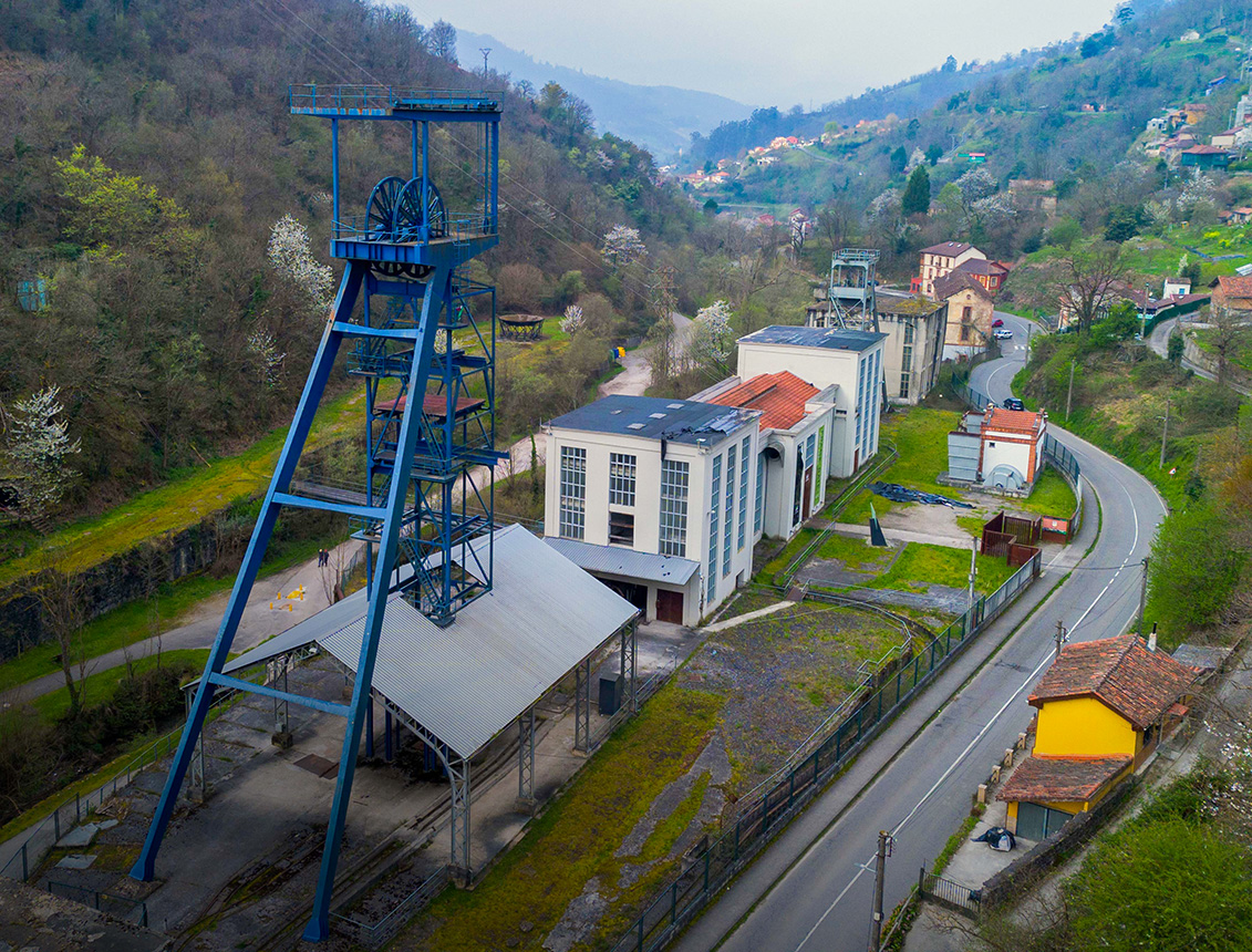 Vista aérea de un antiguo complejo industrial con una estructura de mina y edificios cercanos en un paisaje montañoso