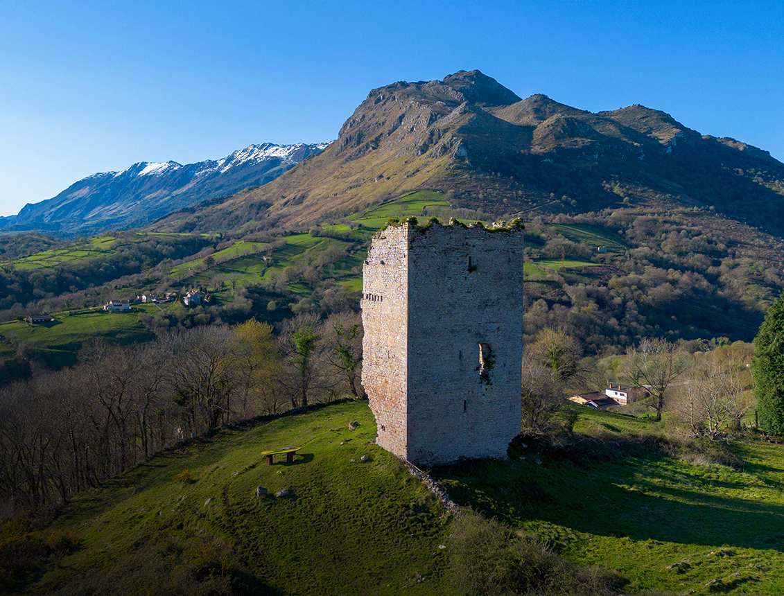 Torre de piedra en un paisaje montañoso con vegetación y un cielo despejado
