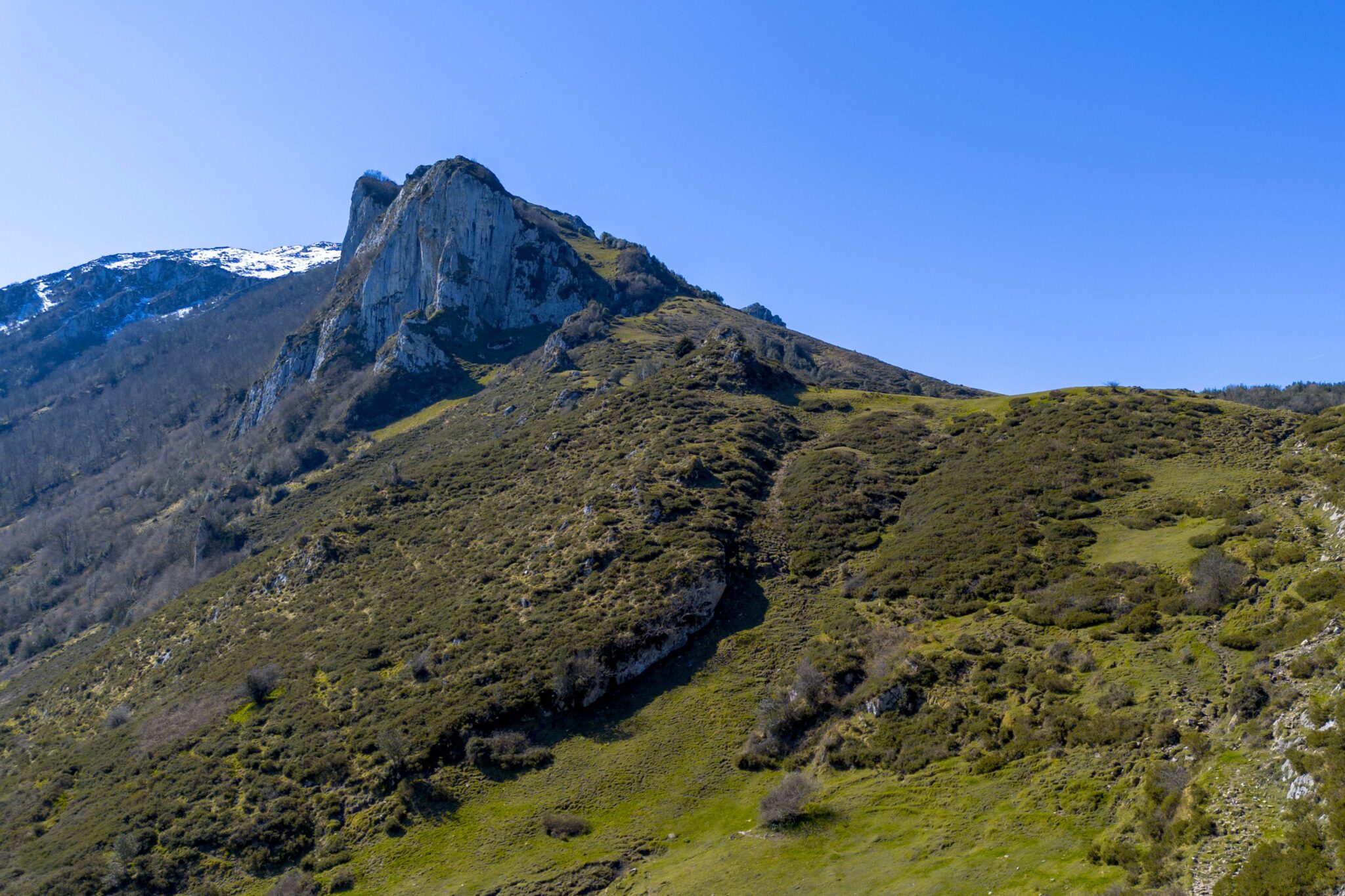Montaña con cumbres rocosas y vegetación verde bajo un cielo despejado
