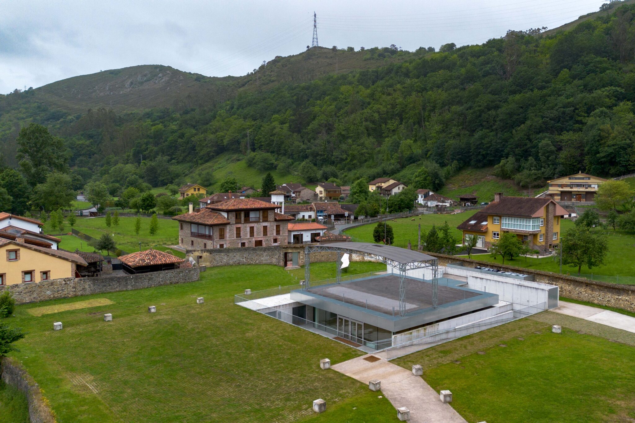 Vista aérea de un edificio moderno rodeado de casas rurales y montañas verdes