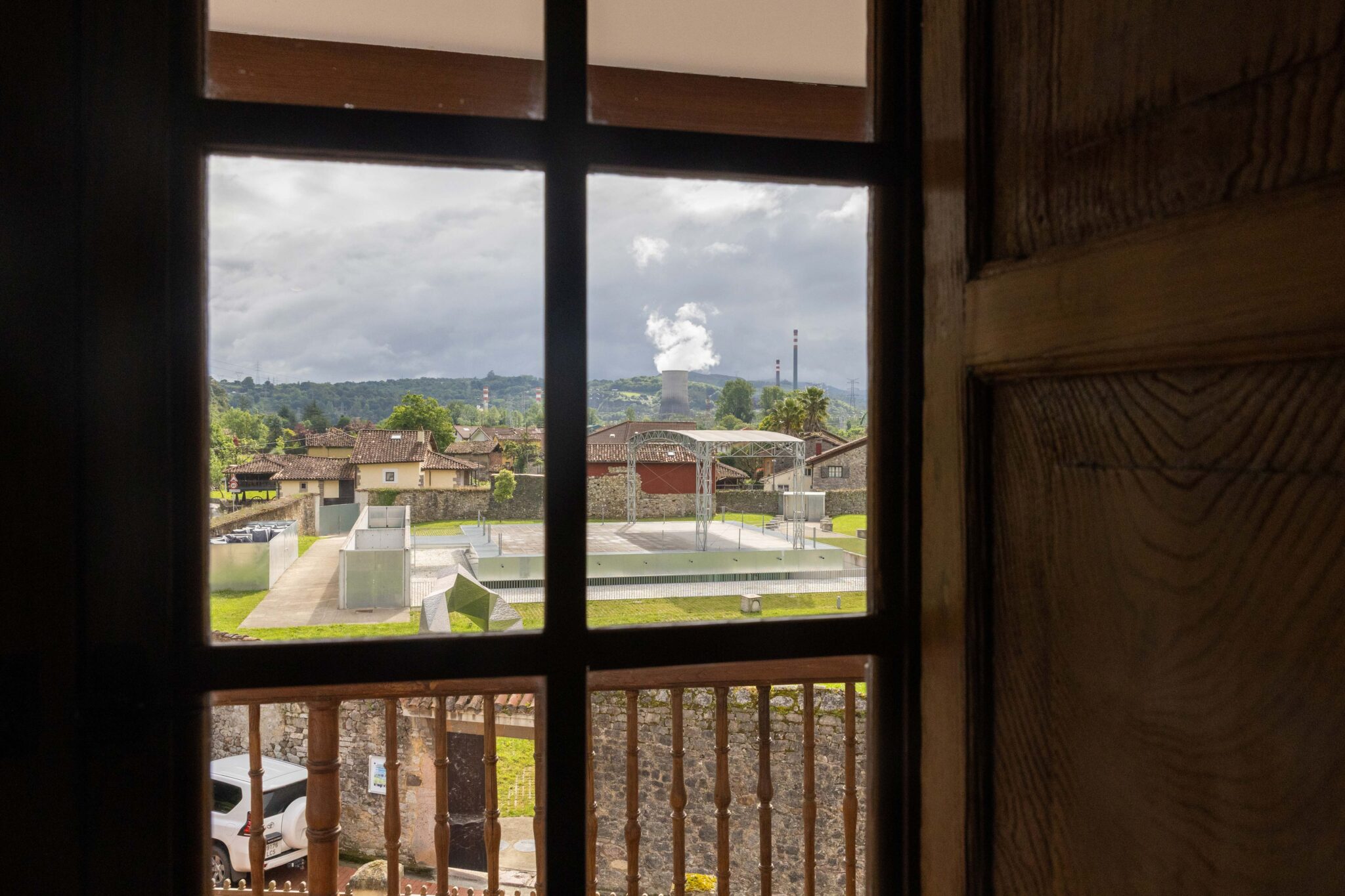 Vista desde una ventana que muestra un paisaje con edificios, un área verde y nubes en el cielo