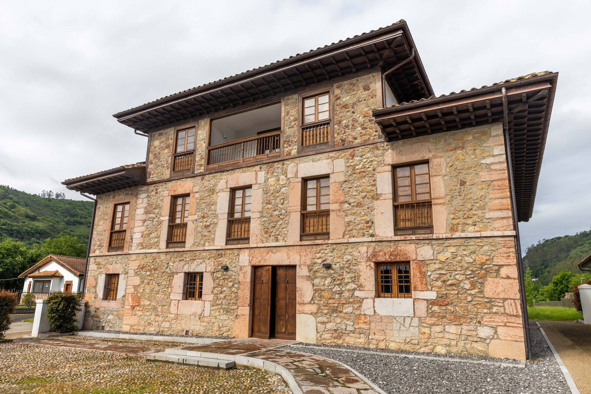 Edificio de tres plantas con fachada de piedra y ventanas de madera en un entorno rural