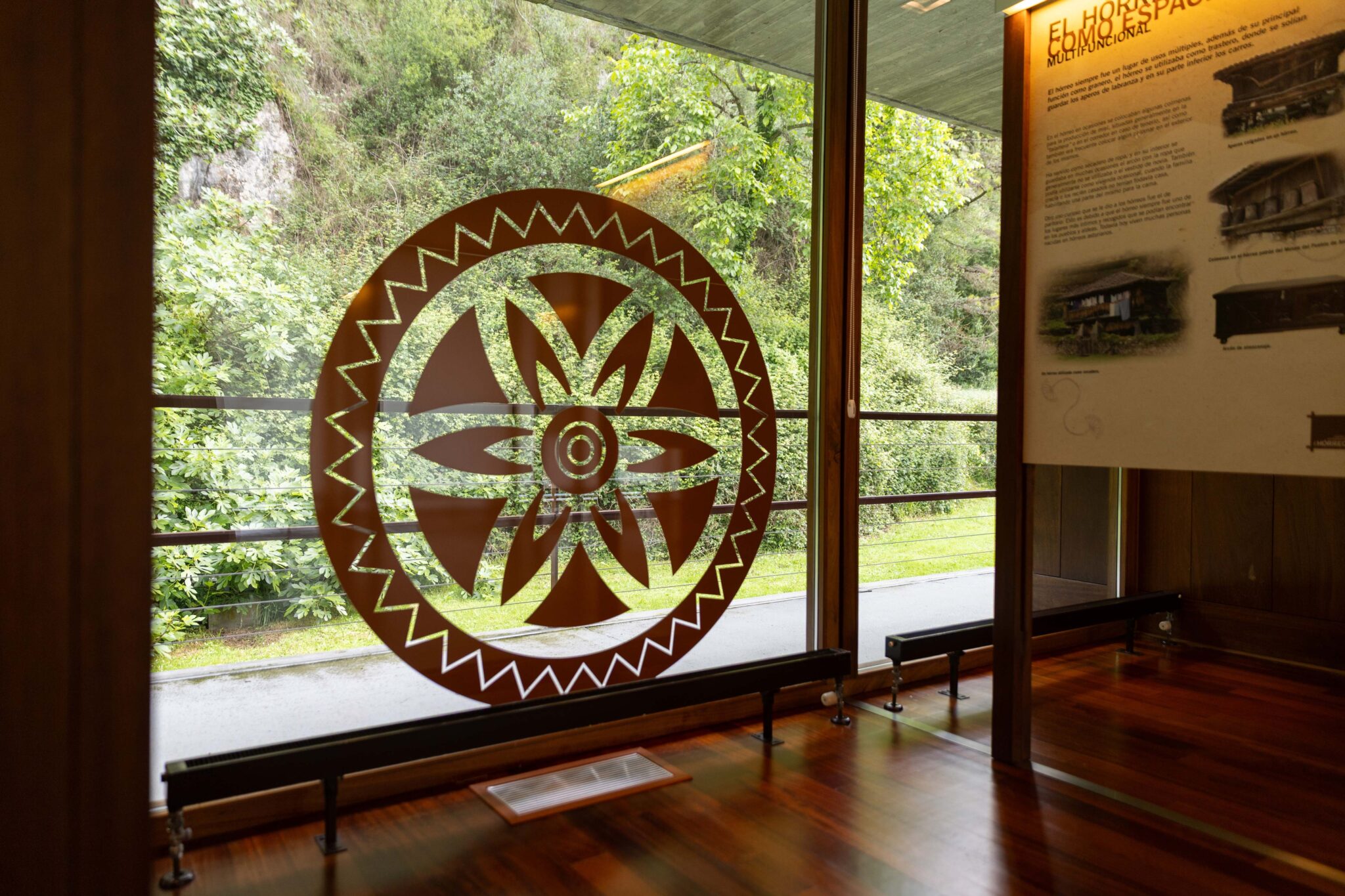 Ventana con un diseño circular en madera que muestra un patrón geométrico, rodeada de vegetación exterior