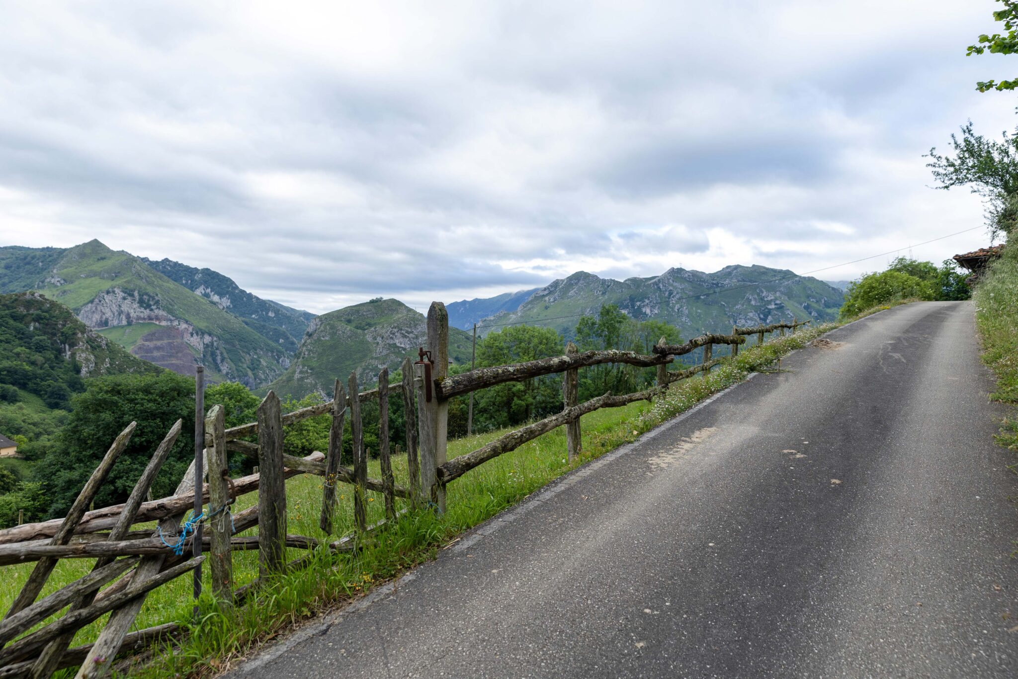 Camino rural rodeado de montañas y una cerca de madera en un paisaje verde