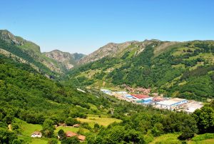 Vista panorámica de un valle montañoso con vegetación y edificios industriales en el fondo