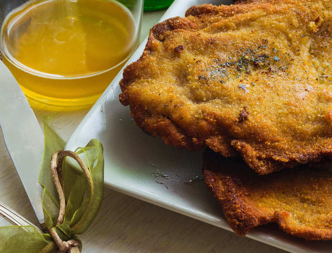 Filetes empanizados dorados servidos en un plato con un recipiente de aceite al lado