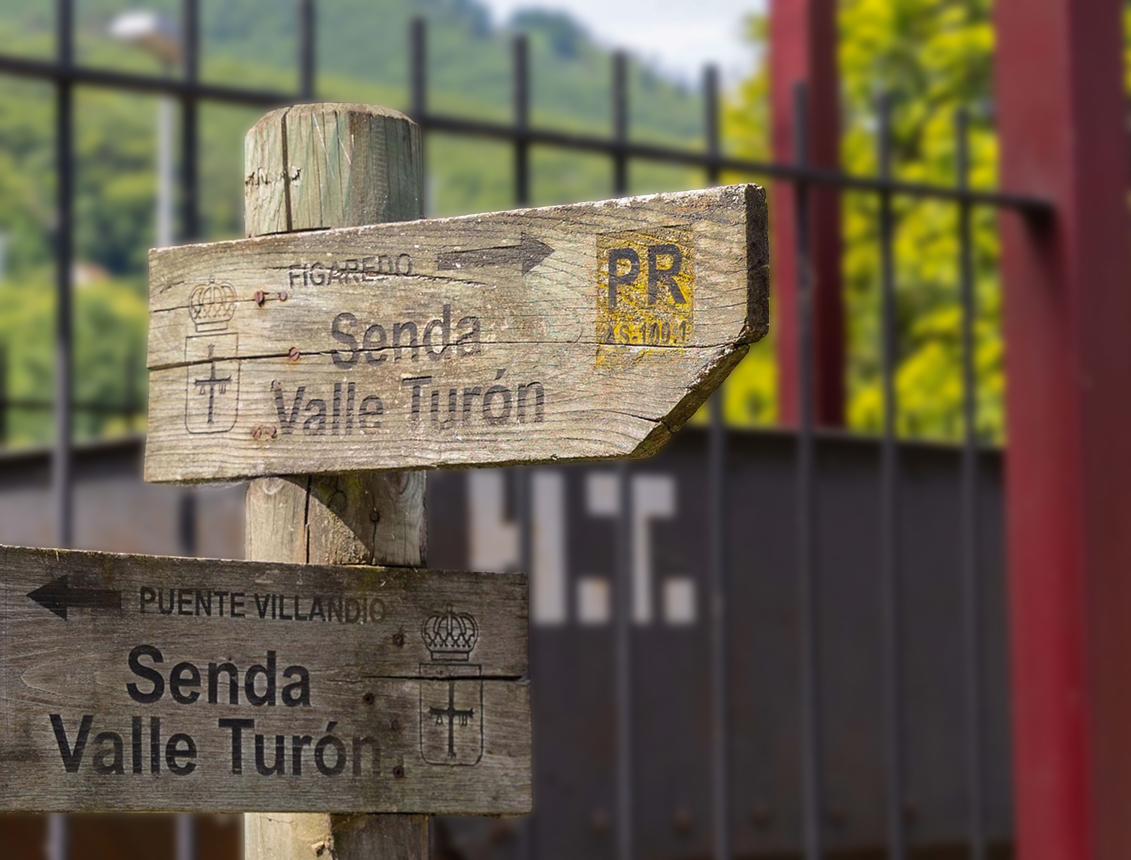 Señalización de madera indicando direcciones hacia Senda Valle-Turón y Puente Vilardonga