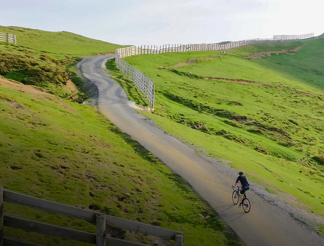 Ciclista pedaleando por un camino sinuoso en un paisaje verde y montañoso