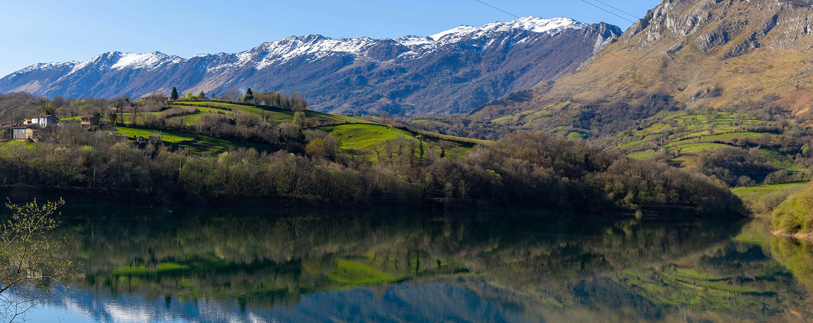 Paisaje montañoso con vegetación verde y un lago reflejando las montañas nevadas al fondo en