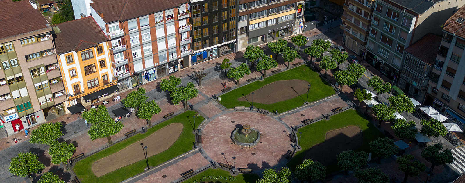 Vista aérea de una plaza con áreas verdes, caminos de piedra y edificios alrededor
