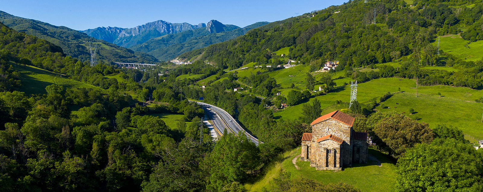 Iglesia en un paisaje montañoso con vegetación verde y una carretera que atraviesa el valle