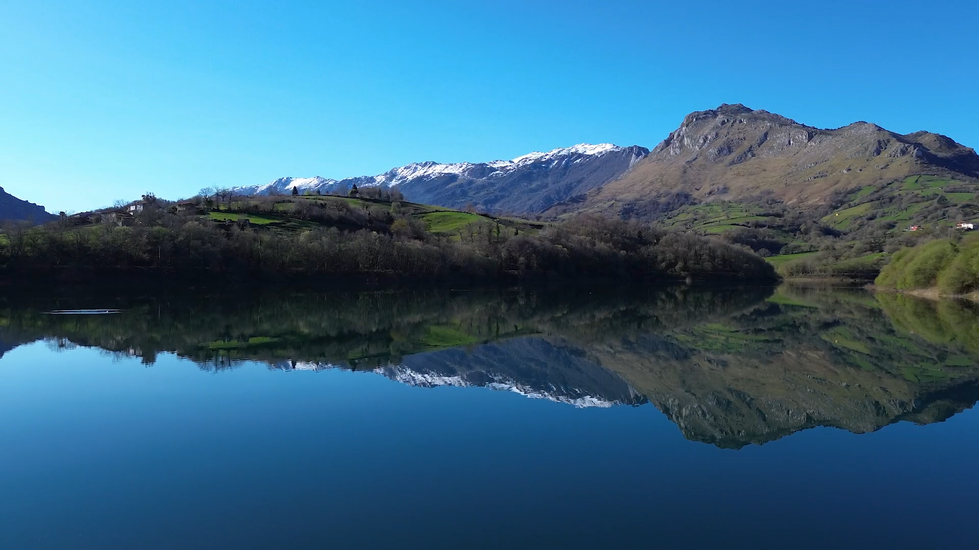 Paisaje montañoso con reflejo en un lago, cielo despejado y vegetación verde